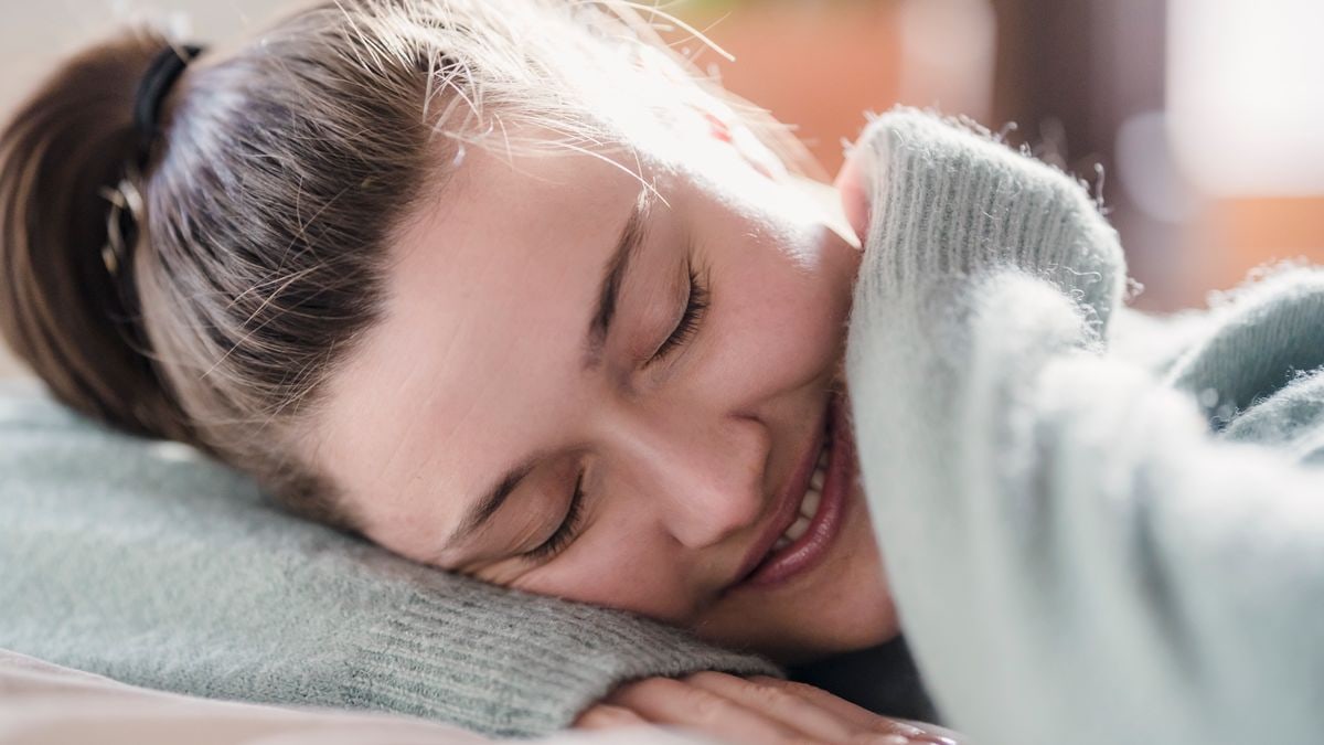 Happy female with closed eyes putting head on hand and smiling while sleeping during weekend morning at home