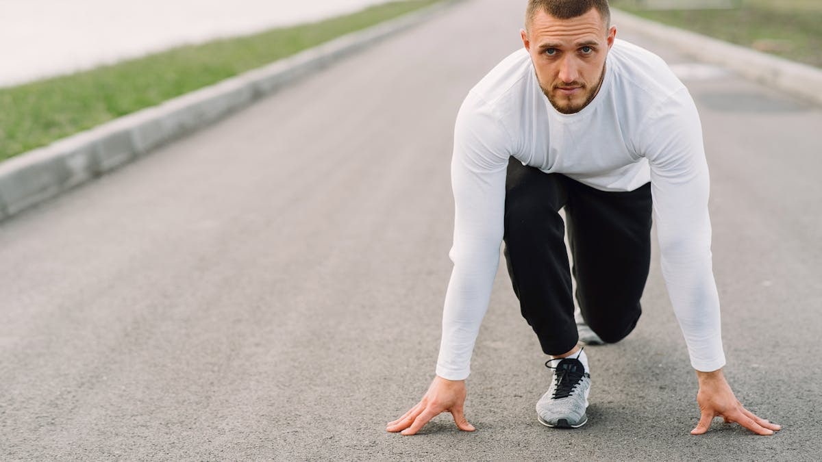 A man in sportswear prepares to run on an empty road, embodying fitness and determination.