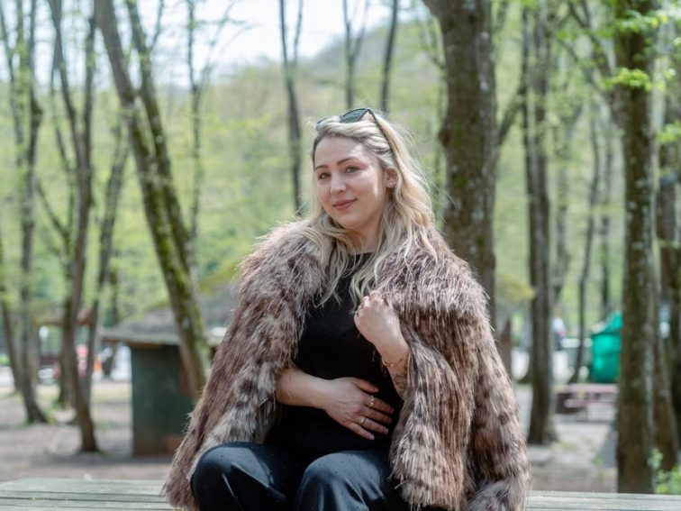 A woman in a fur coat enjoys a serene moment in a forest during springtime.